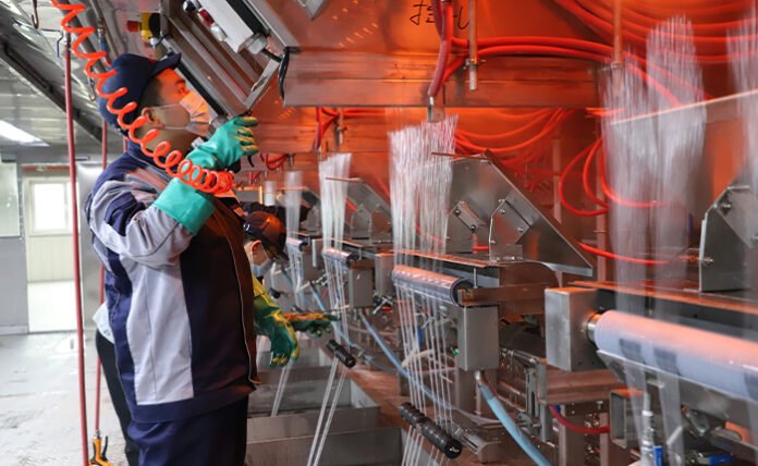 Technician monitoring molten glass fiber filaments during industrial production.